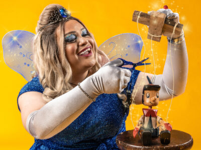 Image of Jthan as the blue fairy snipping the strings from a wooden Pinocchio puppet
