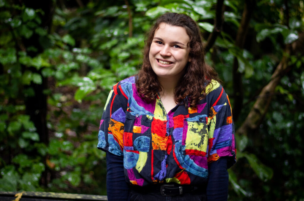 Rebekah de Roo smiling wearing a colourful shirt in front of some trees