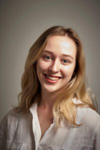 Anna Barker is smiling in front of a grey background