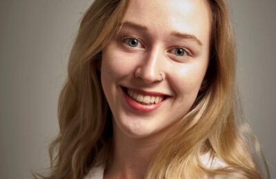 Anna Barker is smiling in front of a grey background